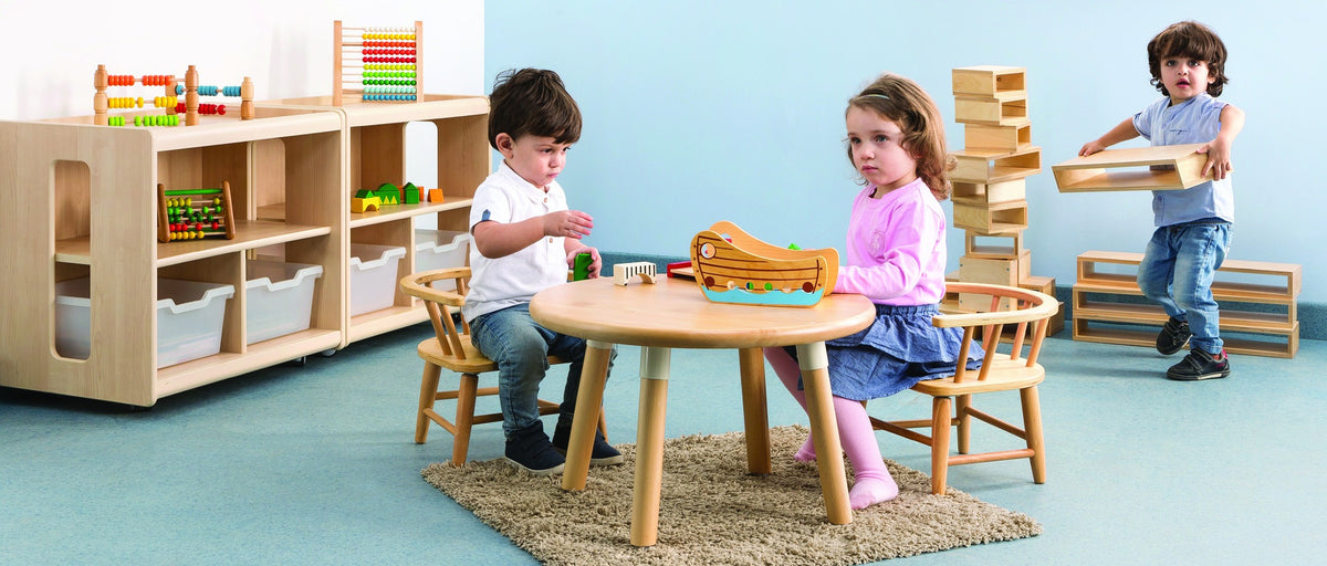 Children playing at a low round table, with open shelves and wooden learning materials.
