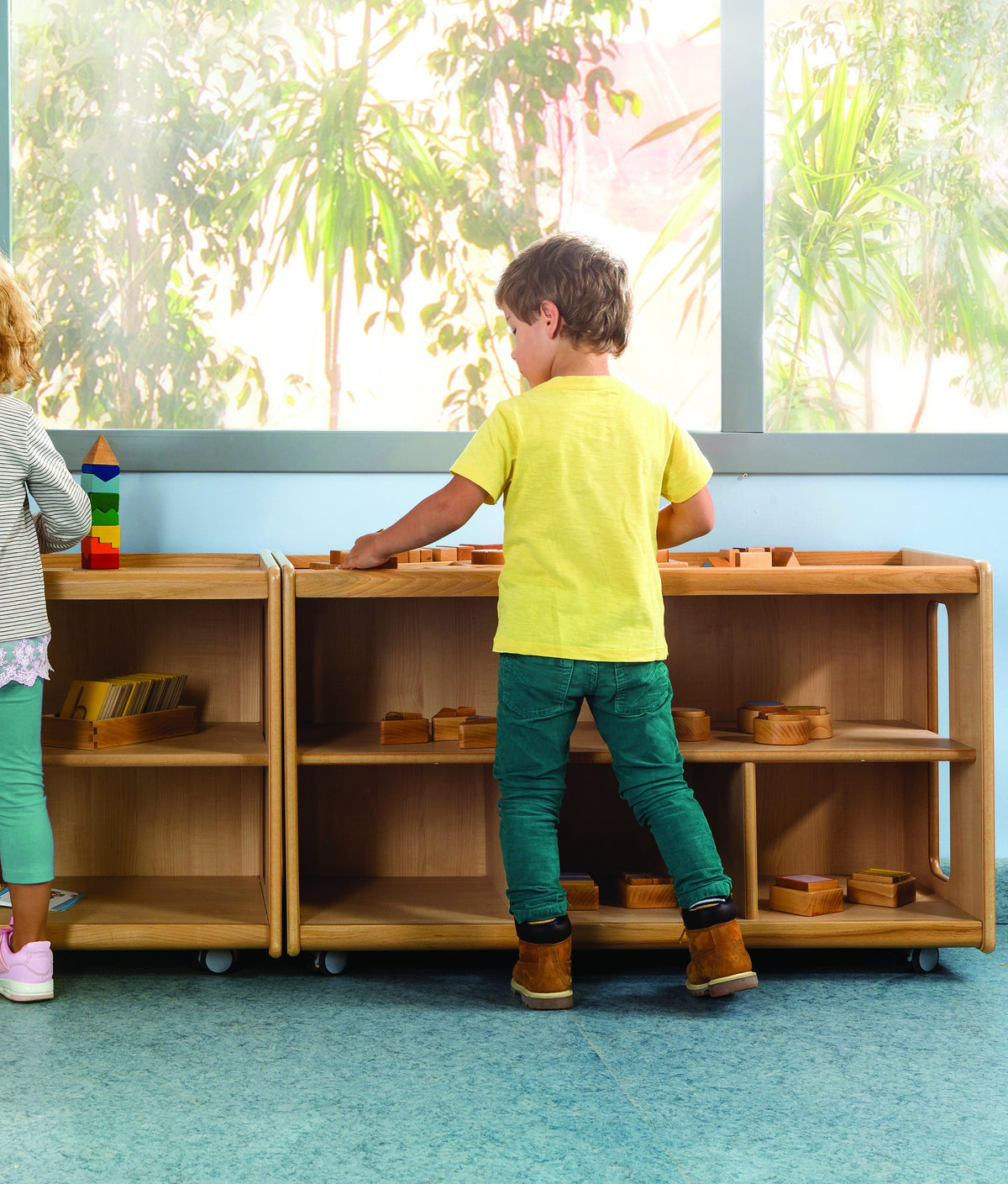 Child exploring a toy on top of low open shelves filled with wooden learning materials.
