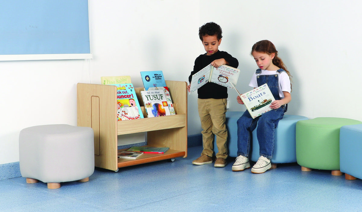 Two children choosing and reading books beside an accessible wooden book browser.