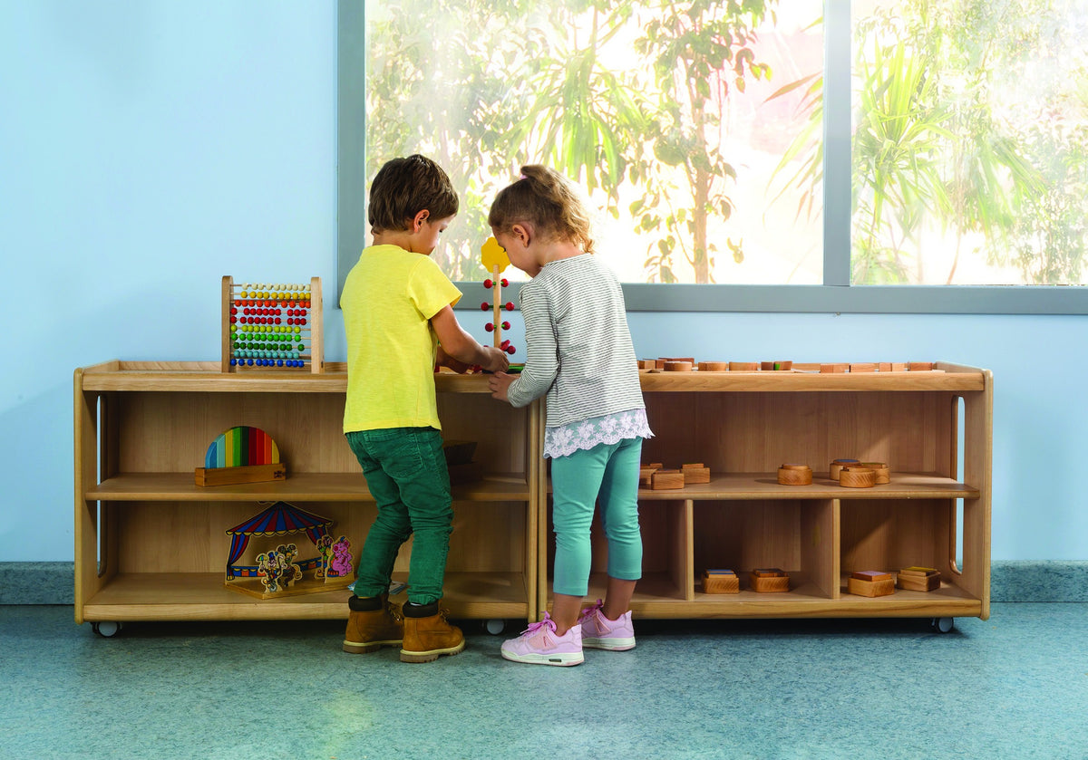 Two children exploring materials at a low open storage shelf.