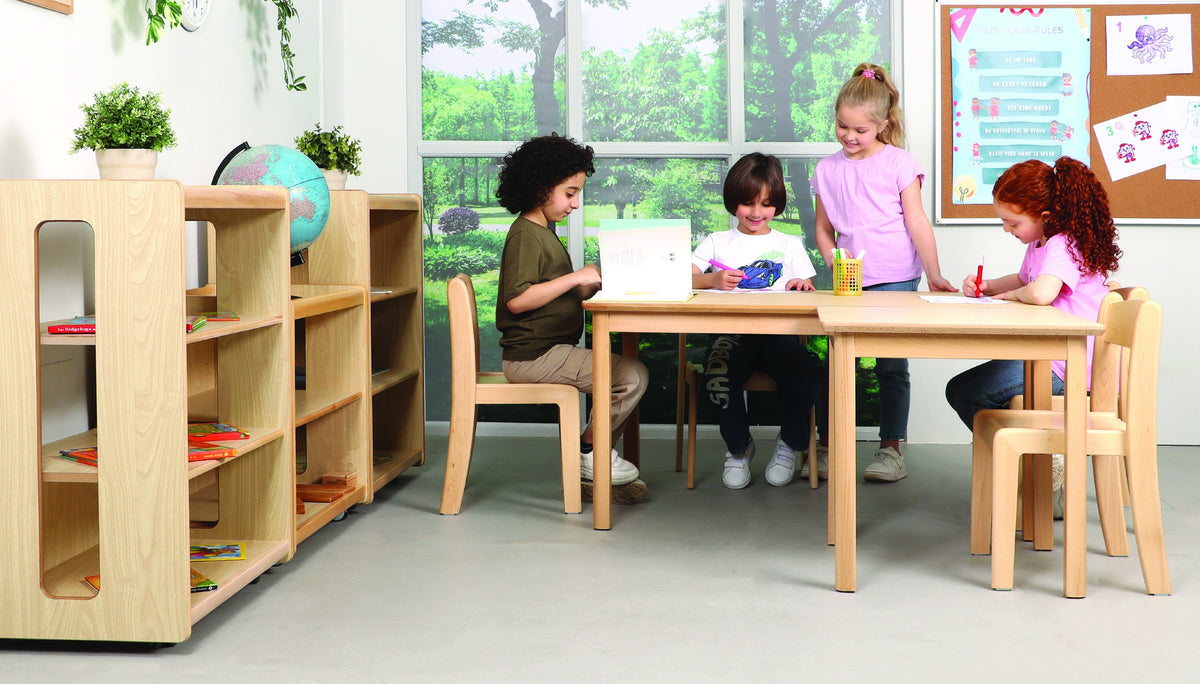 Children sharing a wooden table in a classroom with low open storage.