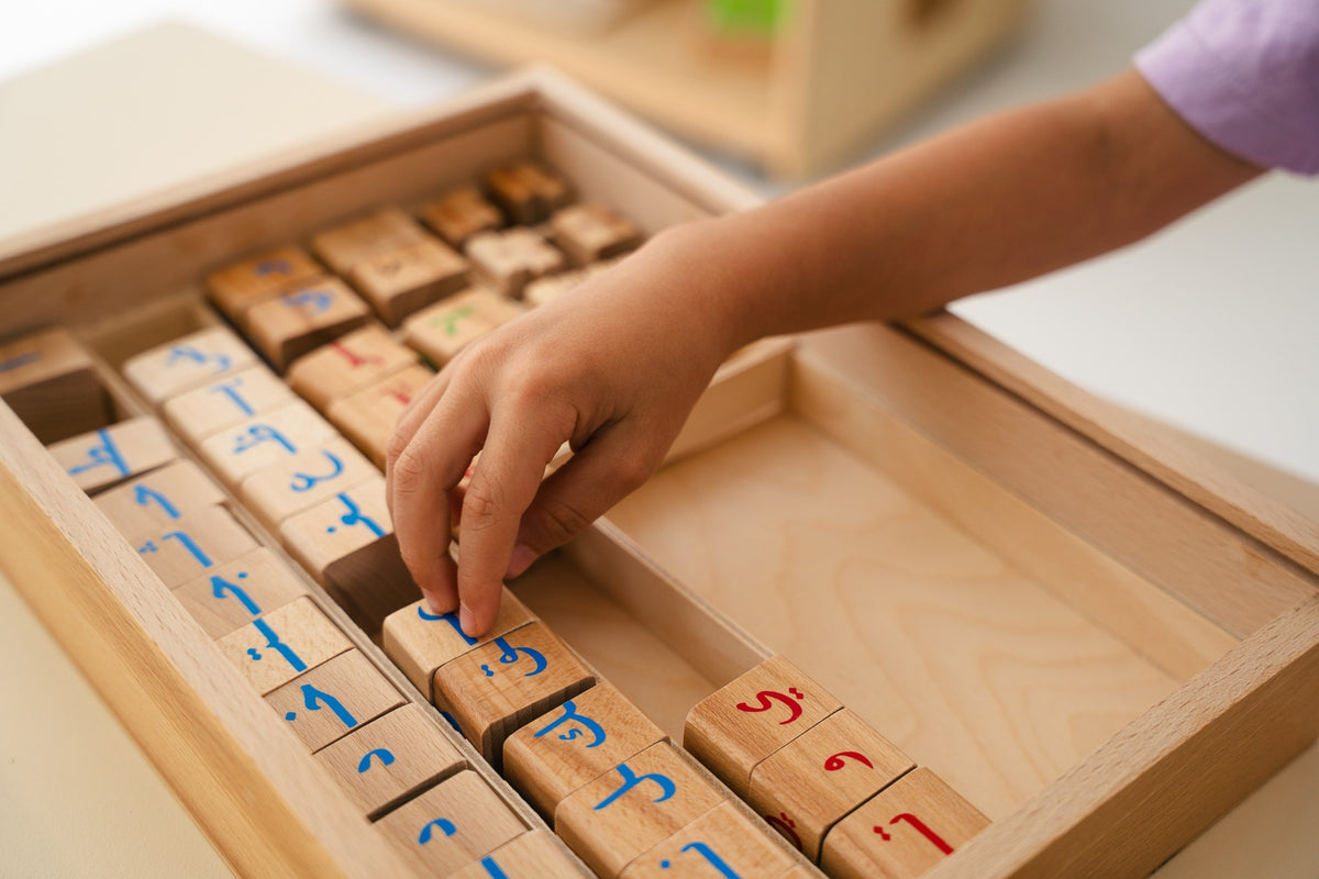 A child selecting a wooden Arabic letter block from a sorting tray.