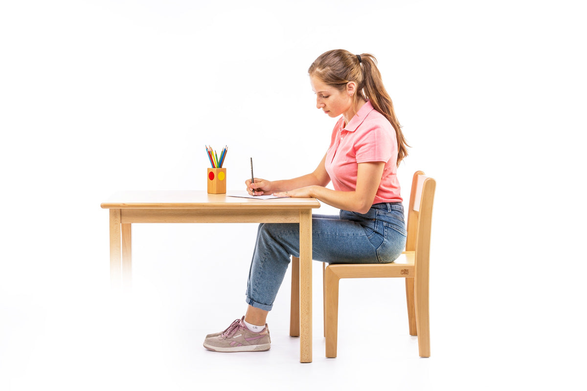 Side view of a child drawing at a wooden table and chair.