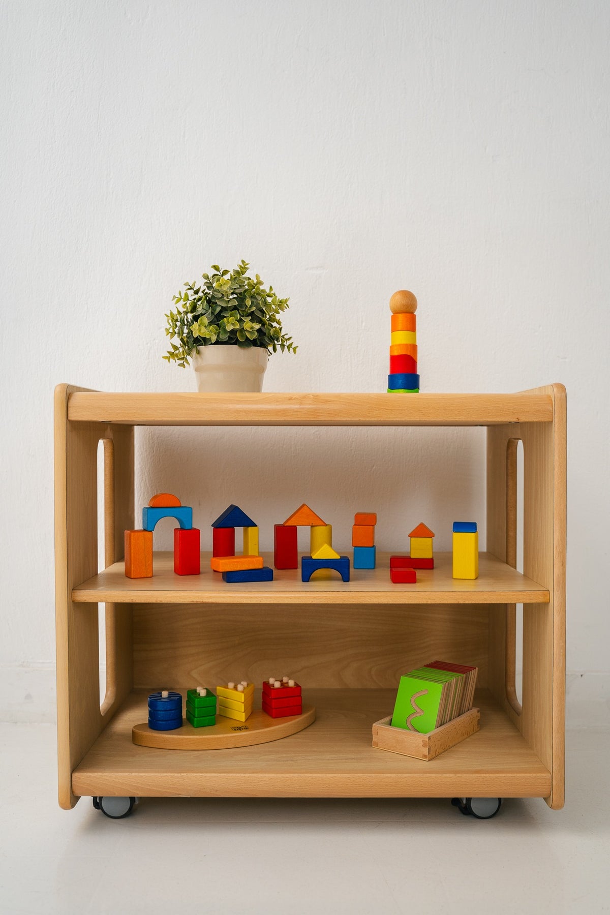 A low wooden shelf displaying blocks, a ring stacker and a shape sorter.