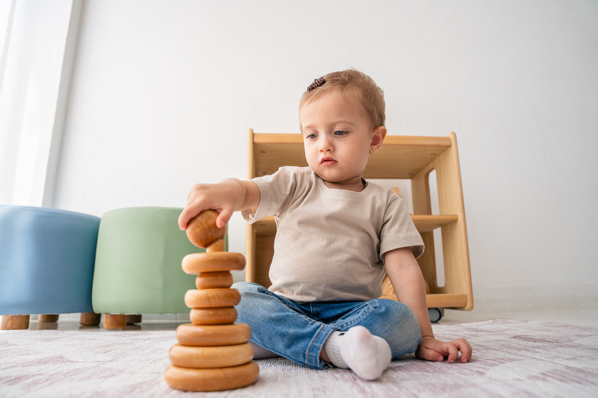 A toddler stacking natural wooden rings on the floor.