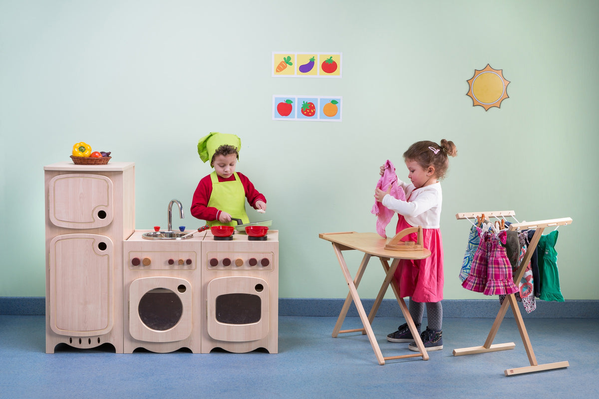 Children playing with a wooden kitchen, ironing table and dress-up rack.