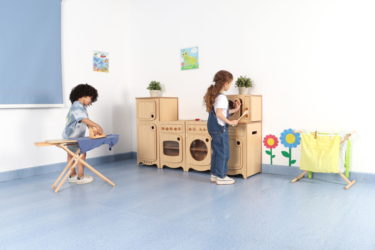 Children exploring a wooden play kitchen and ironing station in a room.