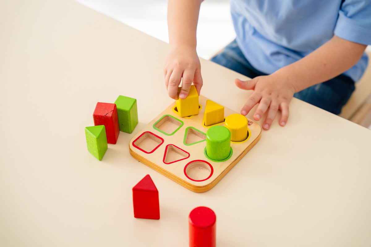 A child matching colourful wooden shapes to their outlined spaces.