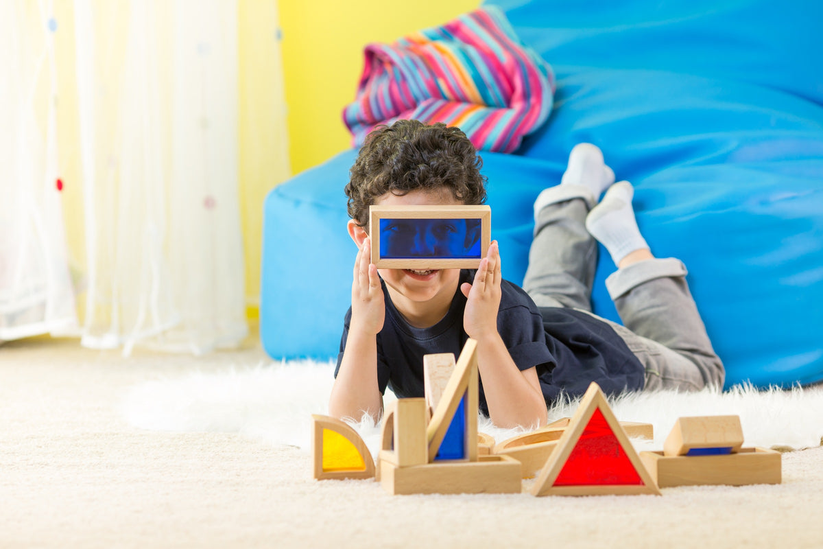 A child looking through a coloured translucent block beside a wooden construction.