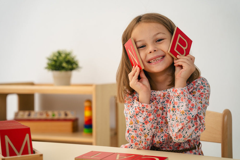 Smiling girl holding red wooden letter cards beside beech shelving