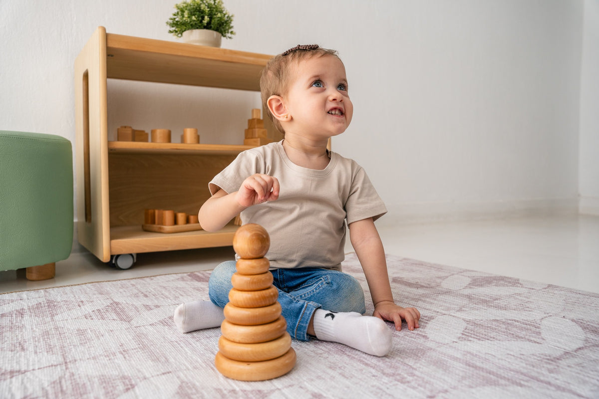 A toddler sitting on the floor with a natural wooden ring stacker